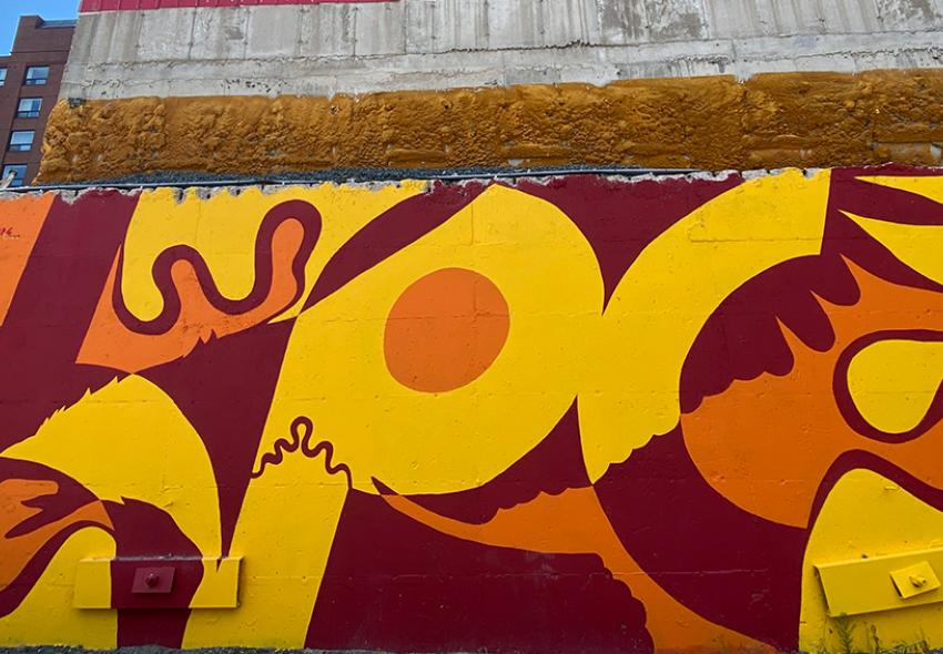 Mural on Grafton Street, titled "Mikisew" by Ininew and Anishinaabe artist Peatr Thomas. Abstract lines, an eagle, and Ininew syllabics are depicted in the mural in red, orange, and yellow colours.