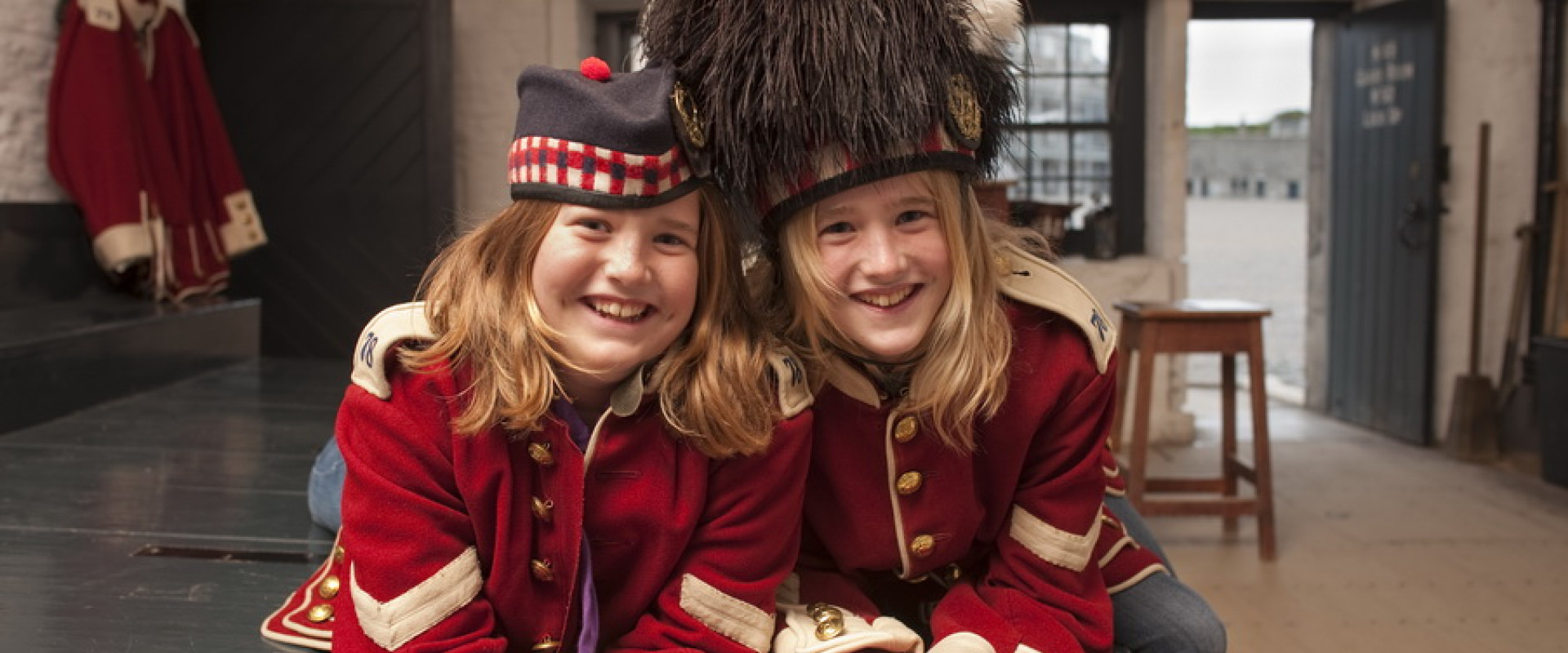 Two girls dressed in red soldier doublets in historic room inside fort.