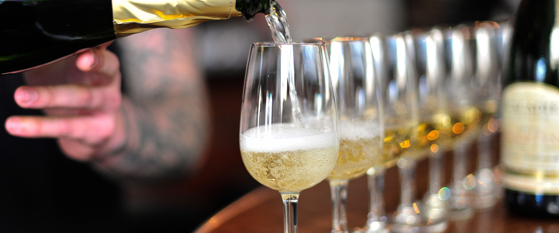 Someone pouring wine into a row of glasses.