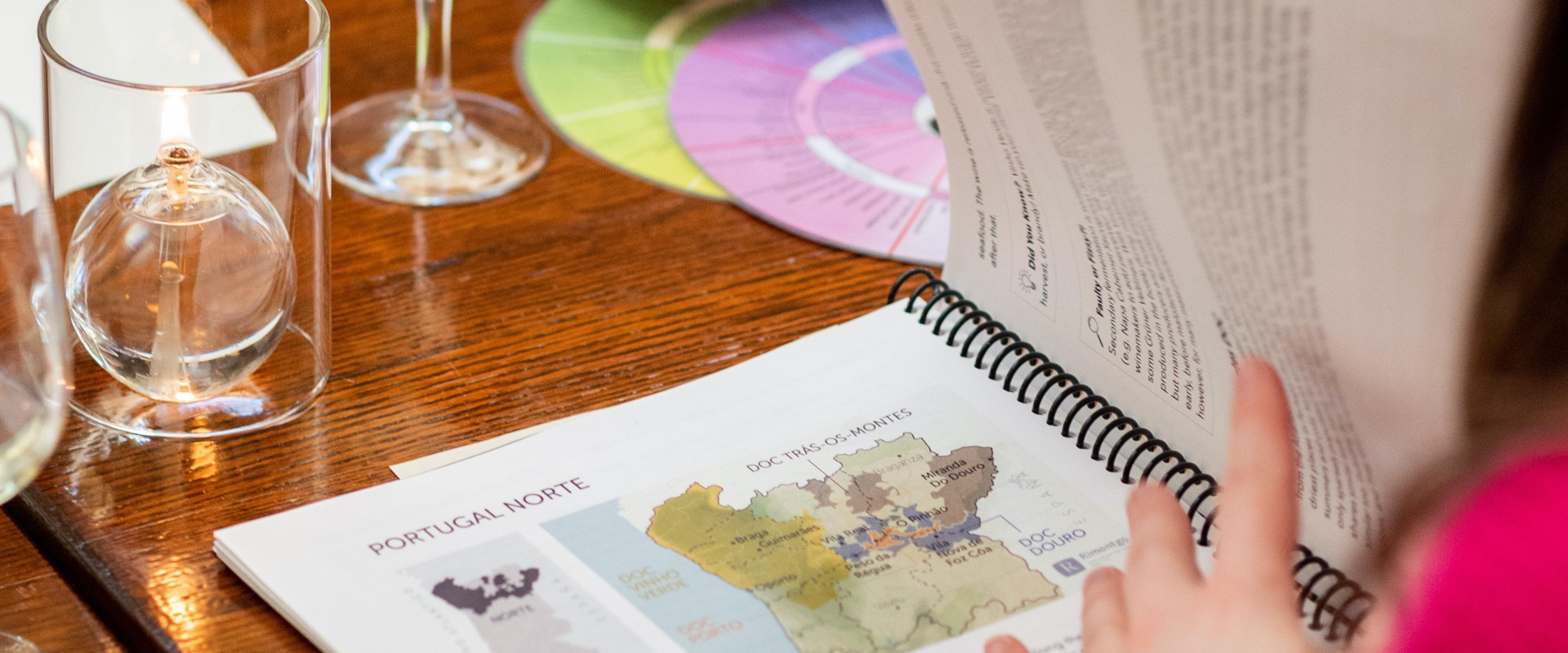 Looking over someone's shoulder at a course booklet and glass of white wine on the table.