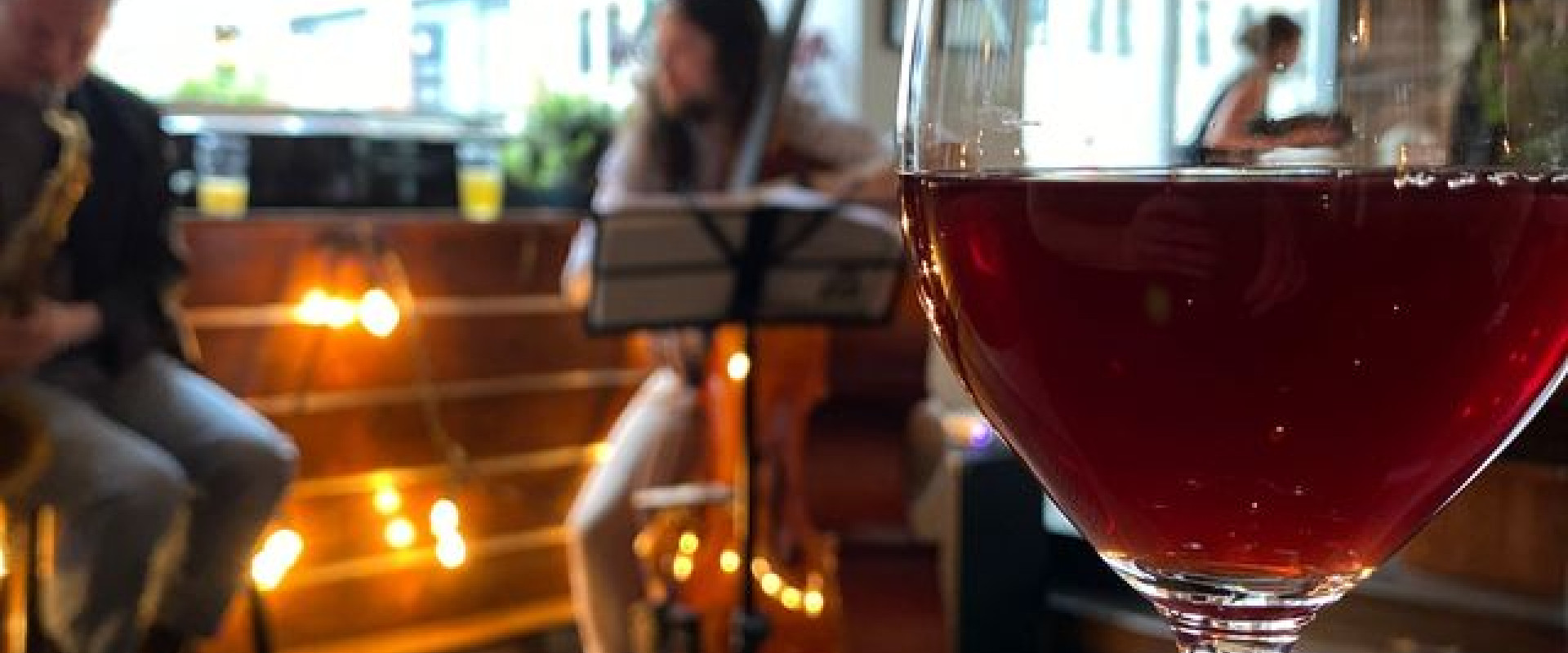Glass of wine on the bar with musicians in the background.