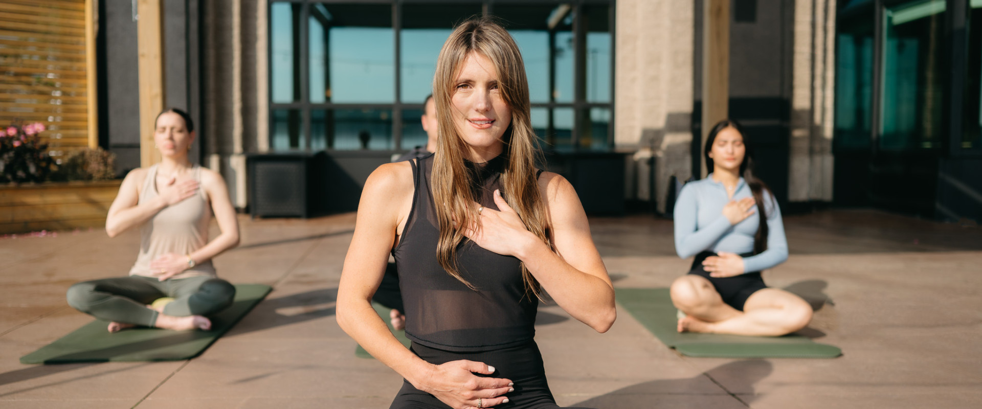 Meditation instructor and guests seated on waterfront patio at sunrise, focus on breathing