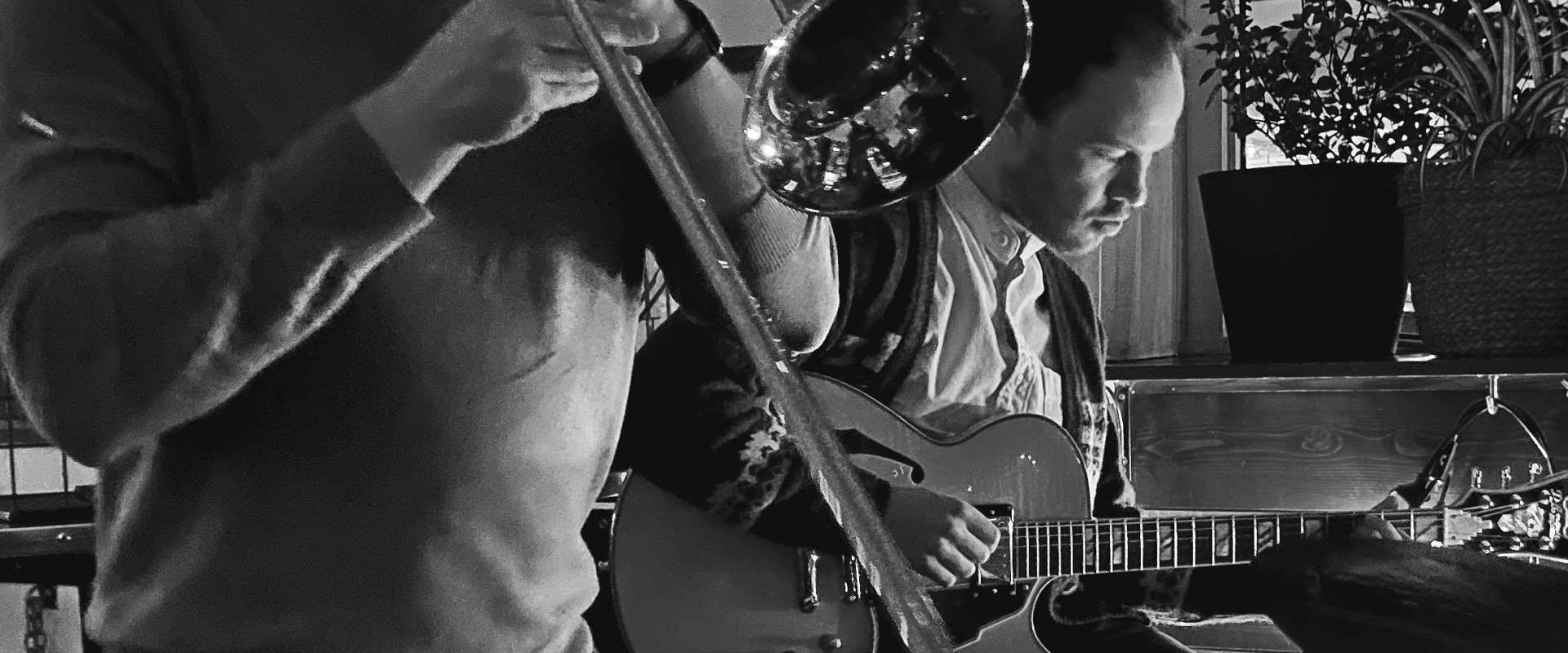 Black and white photo of trombone player with piano player in background 