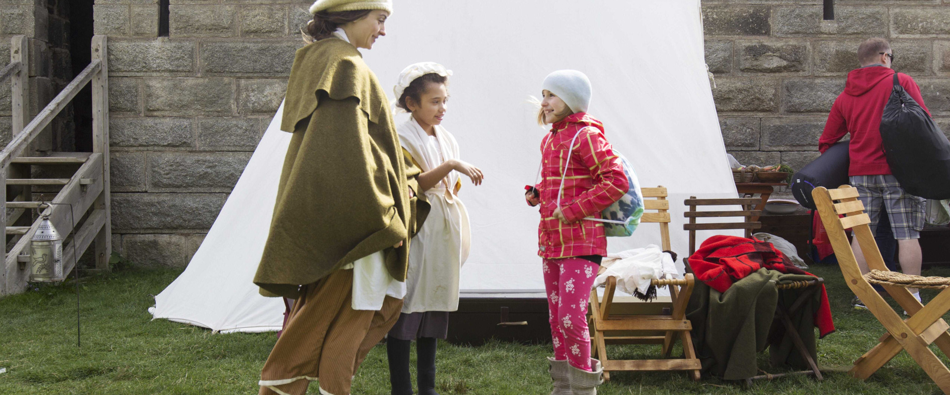 Two individuals in period costume talking to a young child in front of the 17th Century War Encampment tent and chairs in the ditch of the Halifax Citadel National Historic Site.