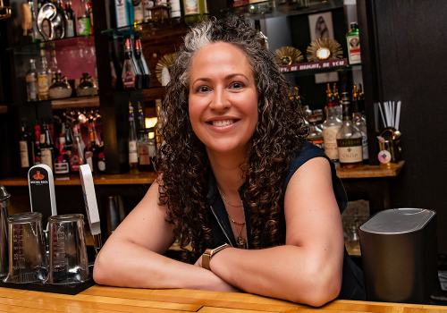 Elle Planetta, owner of Elle's Bistro, smiling for the camera behind the bar in Elle's Bistro