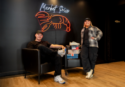 Lauren and Matt, co-owners of Market Price posing in front of their in-store neon sign 