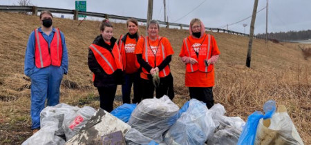 People in orange vest standing by lots of trash bags.